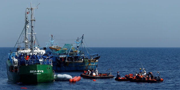 Ein grünes Fischkutter-ähnliches Schiff auf offener See, neben zwei Schlauchbooten und einem weiteren Fischkutter Ein grünes Fischkutter-ähnliches Schiff auf offener See, neben zwei Schlauchbooten und einem weiteren Fischkutter