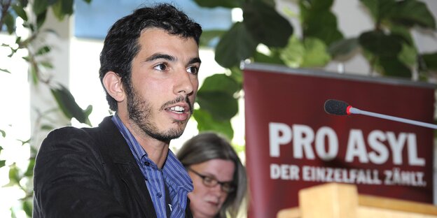Ein junger Mann spricht in ein Mikrofon an einem Rednerpult Ein junger Mann spricht in ein Mikrofon an einem Rednerpult