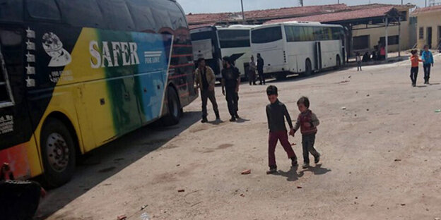 Zwei kleine Kinder gehen Hand in Hand über einen Platz in Richtung eines Busses Zwei kleine Kinder gehen Hand in Hand über einen Platz in Richtung eines Busses