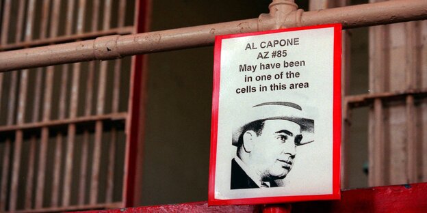 An einem Stahlrohr hängt ein Schild, auf dem steht „Al Capone may have been in one of the cells in this area“, dahinter Gitterstangen An einem Stahlrohr hängt ein Schild, auf dem steht „Al Capone may have been in one of the cells in this area“, dahinter Gitterstangen