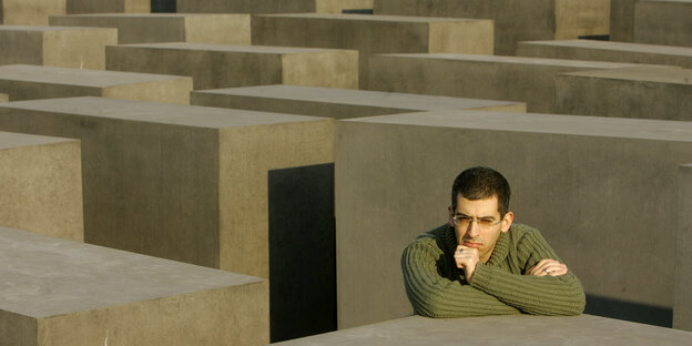 Der Schriftsteller Ori Ginat stützt sieine Arme nachdenklich auf eine der Stelen im Berliner Holocaust-Mahnmal