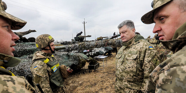 Petro Poroschenko steht neben Soldaten, sie alle tragen Uniformen, hinter ihnen stehen Panzer Petro Poroschenko steht neben Soldaten, sie alle tragen Uniformen, hinter ihnen stehen Panzer