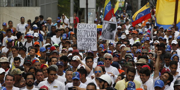 Eine Gruppe von Demonstranten mit Fahnen Venezuelas, in der Mitte ein Schild mit der Aufschrift "Das ist die Diktatur von der Chavez und Fidel träumten" auf Spanisch. Eine Gruppe von Demonstranten mit Fahnen Venezuelas, in der Mitte ein Schild mit der Aufschrift "Das ist die Diktatur von der Chavez und Fidel träumten" auf Spanisch.