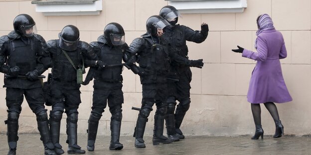 Eine Frau in violettem Mantel diskutiert mit sechs voll gepanzerten Polizisten am Rande der Proste vom 23. März 2017 in Minsk Eine Frau in violettem Mantel diskutiert mit sechs voll gepanzerten Polizisten am Rande der Proste vom 23. März 2017 in Minsk