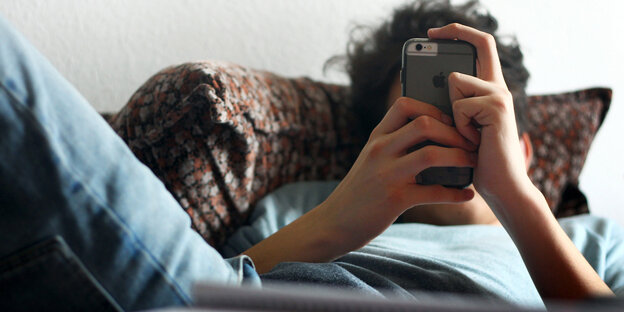 Ein Mann liegt im Bett und hält ein Handy in den Händen, sein Gesicht ist davon verdeckt Ein Mann liegt im Bett und hält ein Handy in den Händen, sein Gesicht ist davon verdeckt