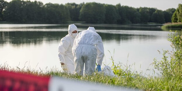 Zwei Menschen in weißen Ganzkörperoveralls an einem Seeufer Zwei Menschen in weißen Ganzkörperoveralls an einem Seeufer