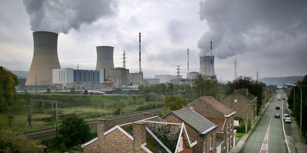 Im Hintergrund Kühltürme eines AKW mit großen Dampfwolken. Im Vordergrund ein paar Häuser und eine Straße. Im Hintergrund Kühltürme eines AKW mit großen Dampfwolken. Im Vordergrund ein paar Häuser und eine Straße.