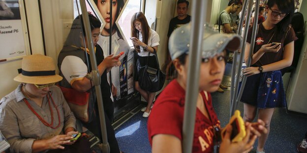 Zahlreiche asiatisch aussehende Menschen in einer Bahn, die alle auf ihre Smartphones schauen Zahlreiche asiatisch aussehende Menschen in einer Bahn, die alle auf ihre Smartphones schauen