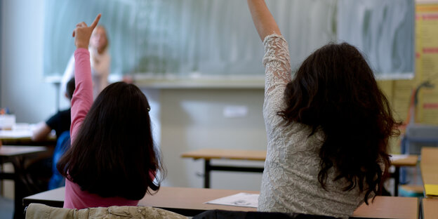 Zwei Mädchen mit dunklen Haaren melden sich in einer Schulstunde Zwei Mädchen mit dunklen Haaren melden sich in einer Schulstunde