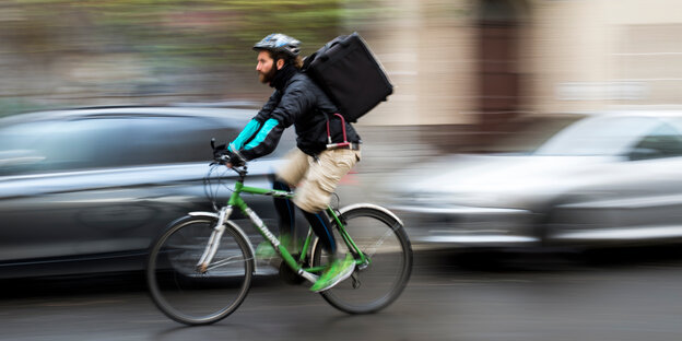 Ein Fahrrad-Essenslieferant fährt mit hoher Geschwindigkeit auf einer Straße Ein Fahrrad-Essenslieferant fährt mit hoher Geschwindigkeit auf einer Straße