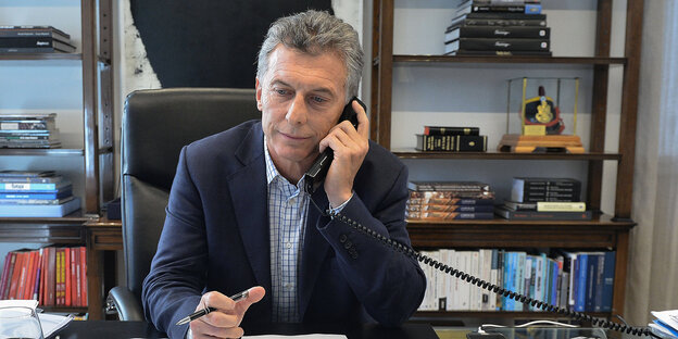 Macri sitzt an seinem Schreibtisch, mit dem Telefonhörer am Ohr, im Hintergrund ein BÜcherregal Macri sitzt an seinem Schreibtisch, mit dem Telefonhörer am Ohr, im Hintergrund ein BÜcherregal