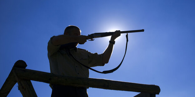 Silhouette eines Jägers mit seinem Gewehr im Anschlag Silhouette eines Jägers mit seinem Gewehr im Anschlag