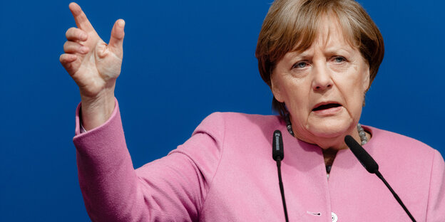 Eine Frau steht an einem Pult und redet. Mit einem Finger zeigt sie nach oben. Eine Frau steht an einem Pult und redet. Mit einem Finger zeigt sie nach oben.