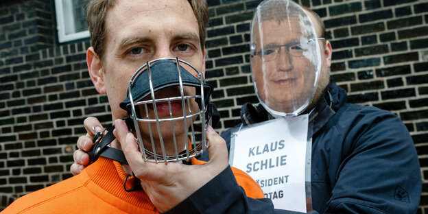 Ein Mann mit Maulkorb und ein Mann mit Maske Ein Mann mit Maulkorb und ein Mann mit Maske