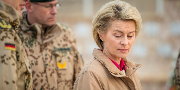 Ursula von der Leyen in sandfarbenem Anorak steht mit gesenktem Kopf vor zwei Soldaten Ursula von der Leyen in sandfarbenem Anorak steht mit gesenktem Kopf vor zwei Soldaten