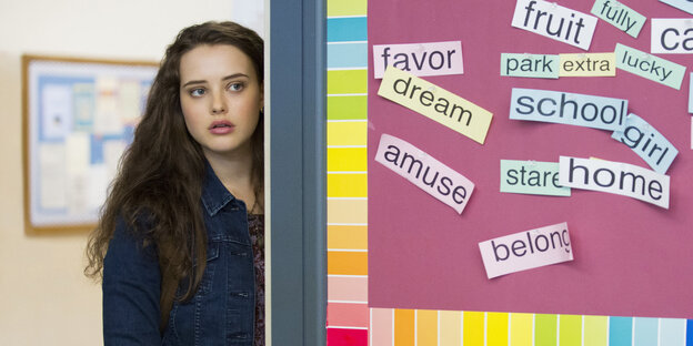Hannah Baker, gespielt von Katherine Langford, steht neben einer Pinnwand in der Schule Hannah Baker, gespielt von Katherine Langford, steht neben einer Pinnwand in der Schule