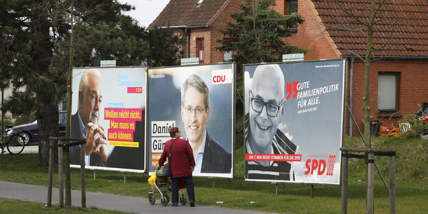 alte Frau vor drei Wahlplakaten an der Straße alte Frau vor drei Wahlplakaten an der Straße