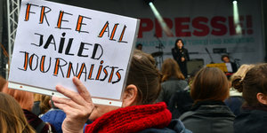 eine Frau hält auf einer Kundgebung ein Schild mit der Aufschrift „Free all jailed journalists“