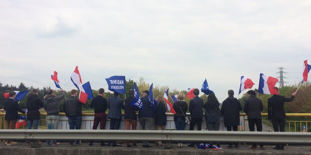 Mehrere junge Menschen stehen nebeneinander am Geländer einer Autobahnbrücke und wehen mit französischen Nationalflaggen Mehrere junge Menschen stehen nebeneinander am Geländer einer Autobahnbrücke und wehen mit französischen Nationalflaggen
