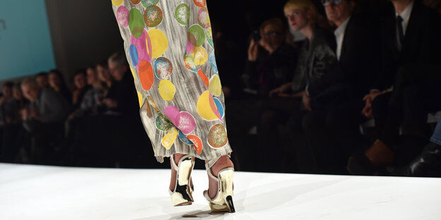 ein Model trägt einen langen bunten Rock und hohe silberne Schuhe auf dem Laufsteg ein Model trägt einen langen bunten Rock und hohe silberne Schuhe auf dem Laufsteg
