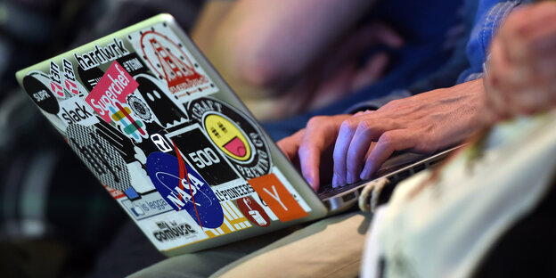 Ein mit vielen Aufklebern verzierter Laptop, auf dem jemand tippt (man sieht nur seine Hände). Ein mit vielen Aufklebern verzierter Laptop, auf dem jemand tippt (man sieht nur seine Hände).