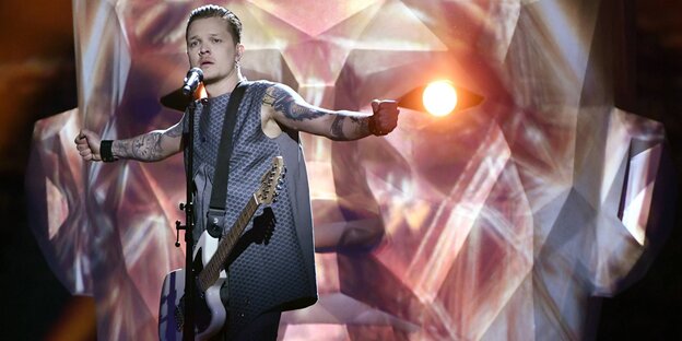 Ein junger Mann hat eine elektronische Gitarre vor seinem Körper und streckt beide Hände zu den Seiten aus Ein junger Mann hat eine elektronische Gitarre vor seinem Körper und streckt beide Hände zu den Seiten aus