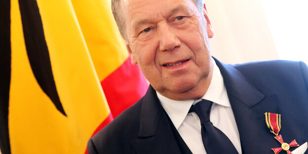 Ein älterer Mann vor einer Deutschlandflagge, an seinem Anzug ein Bundesverdienstkreuz Ein älterer Mann vor einer Deutschlandflagge, an seinem Anzug ein Bundesverdienstkreuz