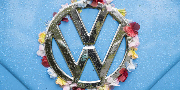 Das Logo eines VW-Autos auf hellblauem Untergrund ist mit Blumenblättern umrundet Das Logo eines VW-Autos auf hellblauem Untergrund ist mit Blumenblättern umrundet