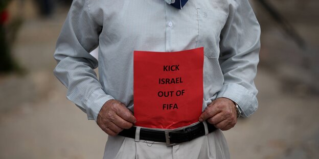 Zu sehen ist der Rumpf eines Manns, der ein Protestschild mit den Worten "Kick Israel out of FIFA" hält Zu sehen ist der Rumpf eines Manns, der ein Protestschild mit den Worten "Kick Israel out of FIFA" hält