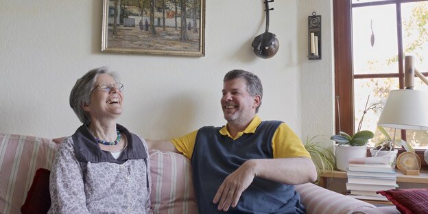 Ein Ehepaar sitzt lachend auf einem Sofa im Wohnzimmer Ein Ehepaar sitzt lachend auf einem Sofa im Wohnzimmer