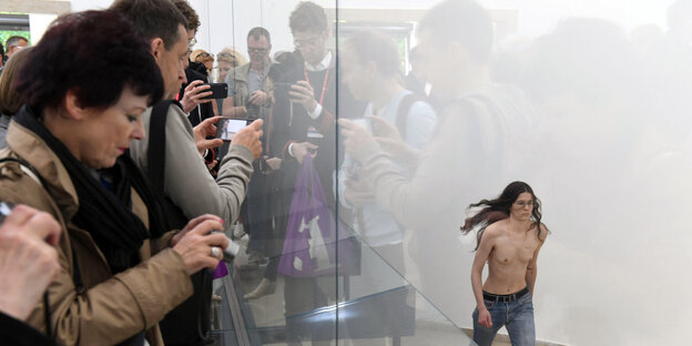 Besucher und Besucherinnen fotografieren eine Frau, die auf der Biennale in Venedig hinter Glas mit nacktem Oberkörper läuft Besucher und Besucherinnen fotografieren eine Frau, die auf der Biennale in Venedig hinter Glas mit nacktem Oberkörper läuft