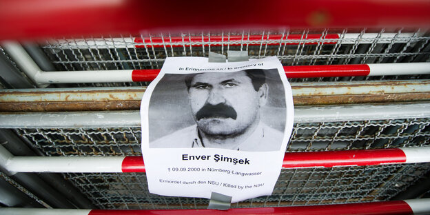 An einem rot-weißen Absperrgitter hängt ein Zettel mit dem Porträt von Enver Şimşek An einem rot-weißen Absperrgitter hängt ein Zettel mit dem Porträt von Enver Şimşek