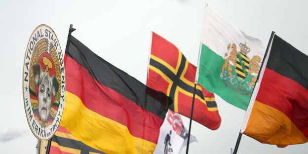 Sächsische Landesflagge, Deutschlandfahne, Fahne mit nationalistischer Symbolik und Anti-Merkel-Plakat Sächsische Landesflagge, Deutschlandfahne, Fahne mit nationalistischer Symbolik und Anti-Merkel-Plakat