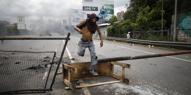 Ein Mann mit vermummtem Gesicht springt über eine Straßensperre in Caracas Ein Mann mit vermummtem Gesicht springt über eine Straßensperre in Caracas