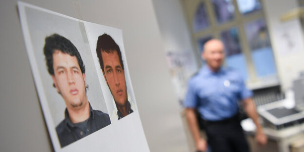 ein Fahndungsfoto von Anis Amri hängt an einer weißen Wand, im Hintergrund ist verschwommen ein Polizist zu sehen ein Fahndungsfoto von Anis Amri hängt an einer weißen Wand, im Hintergrund ist verschwommen ein Polizist zu sehen