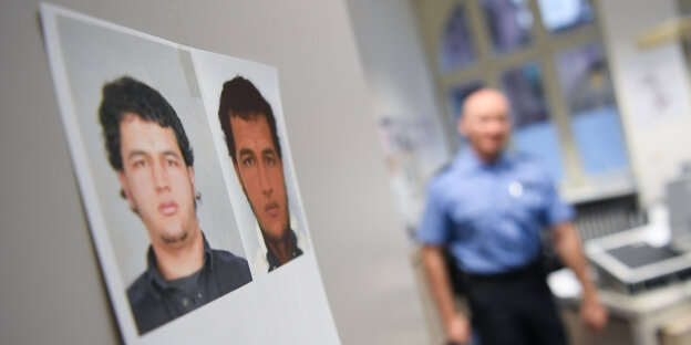 ein Fahndungsfoto von Anis Amri hängt an einer weißen Wand, im Hintergrund ist verschwommen ein Polizist zu sehen