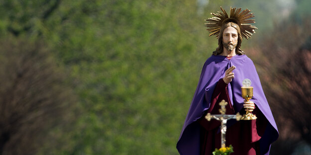 Eine Jesusstatue in lila Umhang vor Bäumen Eine Jesusstatue in lila Umhang vor Bäumen
