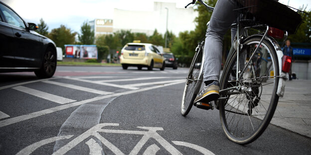 Eine Person auf einem Fahrrad bieg auf einem Radstreifen in einen Kreisverkehr ein, neben ihr fahren Autos Eine Person auf einem Fahrrad bieg auf einem Radstreifen in einen Kreisverkehr ein, neben ihr fahren Autos