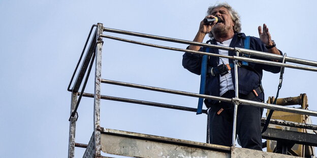 Beppe Grillo schreit in ein Mikrofon, während er auf einem Kran steht Beppe Grillo schreit in ein Mikrofon, während er auf einem Kran steht
