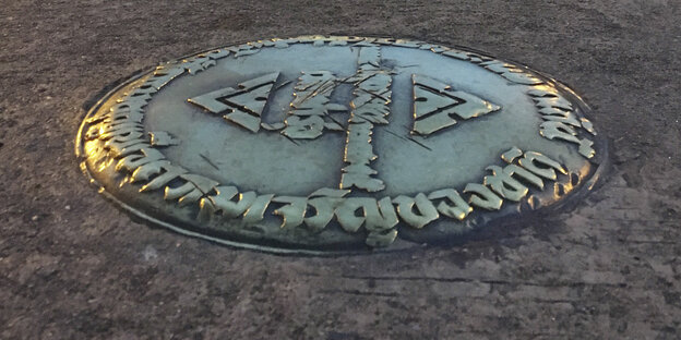 Eine in den Asphalt eingelassene Bronzeplakette Eine in den Asphalt eingelassene Bronzeplakette