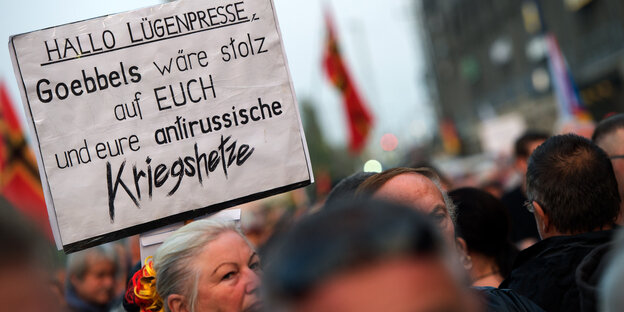 Köpfe auf einer Demo. In Mitten der Menge ein Schild: "Hallo Lügenpresse, Goebbels wäre stolz auf EUCH und eure antirussische Kriegshetze"