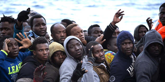 Viele Männer sitzen in einem Boot, einige heben die Hand Viele Männer sitzen in einem Boot, einige heben die Hand