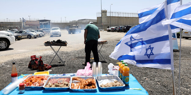 Vor einem Gefängnis in Israel grillt ein Mann neben israelischen Flaggen Vor einem Gefängnis in Israel grillt ein Mann neben israelischen Flaggen