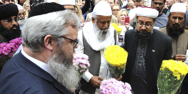 Juden, Christen und Muslime stehen zusammen, sie halten Blumen in den Händen Juden, Christen und Muslime stehen zusammen, sie halten Blumen in den Händen