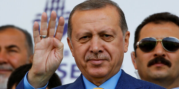 Erdogan hebt die rechte Hand hinter ihm steht ein Mann mit Sonnenbrille Erdogan hebt die rechte Hand hinter ihm steht ein Mann mit Sonnenbrille