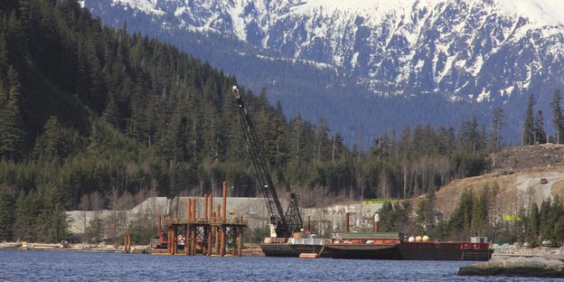 Seeufer am Fuß von Bergen, im Wasser ein Schiff und eine im Bau befindliche Plattform Seeufer am Fuß von Bergen, im Wasser ein Schiff und eine im Bau befindliche Plattform
