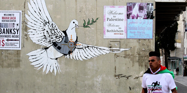 Ein Marathonläufer läuft an einer Wand mit Plakaten vorbei: "Welcome to Palestine" und eine Friedenstaube im Visier Ein Marathonläufer läuft an einer Wand mit Plakaten vorbei: "Welcome to Palestine" und eine Friedenstaube im Visier