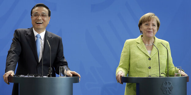 Li Keqiang (li.) und Angela Merkel stehen an Pulten vor blaum Hintergrund Li Keqiang (li.) und Angela Merkel stehen an Pulten vor blaum Hintergrund