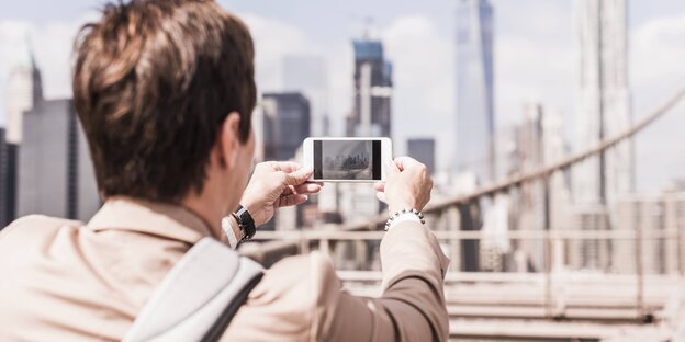 Ein junger Mann fotografiert mit seinem Handy die Skyline von New York Ein junger Mann fotografiert mit seinem Handy die Skyline von New York