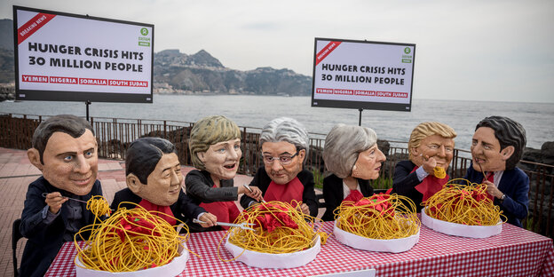 An einem Tisch sitzen Aktivisten, die Masken von Staatschef_innen tragen und Spaghetti essen, dahinter Schilder, auf denen „Hunger crisis“ steht An einem Tisch sitzen Aktivisten, die Masken von Staatschef_innen tragen und Spaghetti essen, dahinter Schilder, auf denen „Hunger crisis“ steht